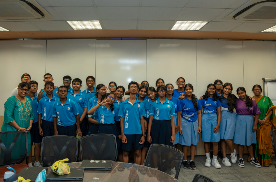 Group of students in blue uniforms pose in a classroom, with three adults at the sides.