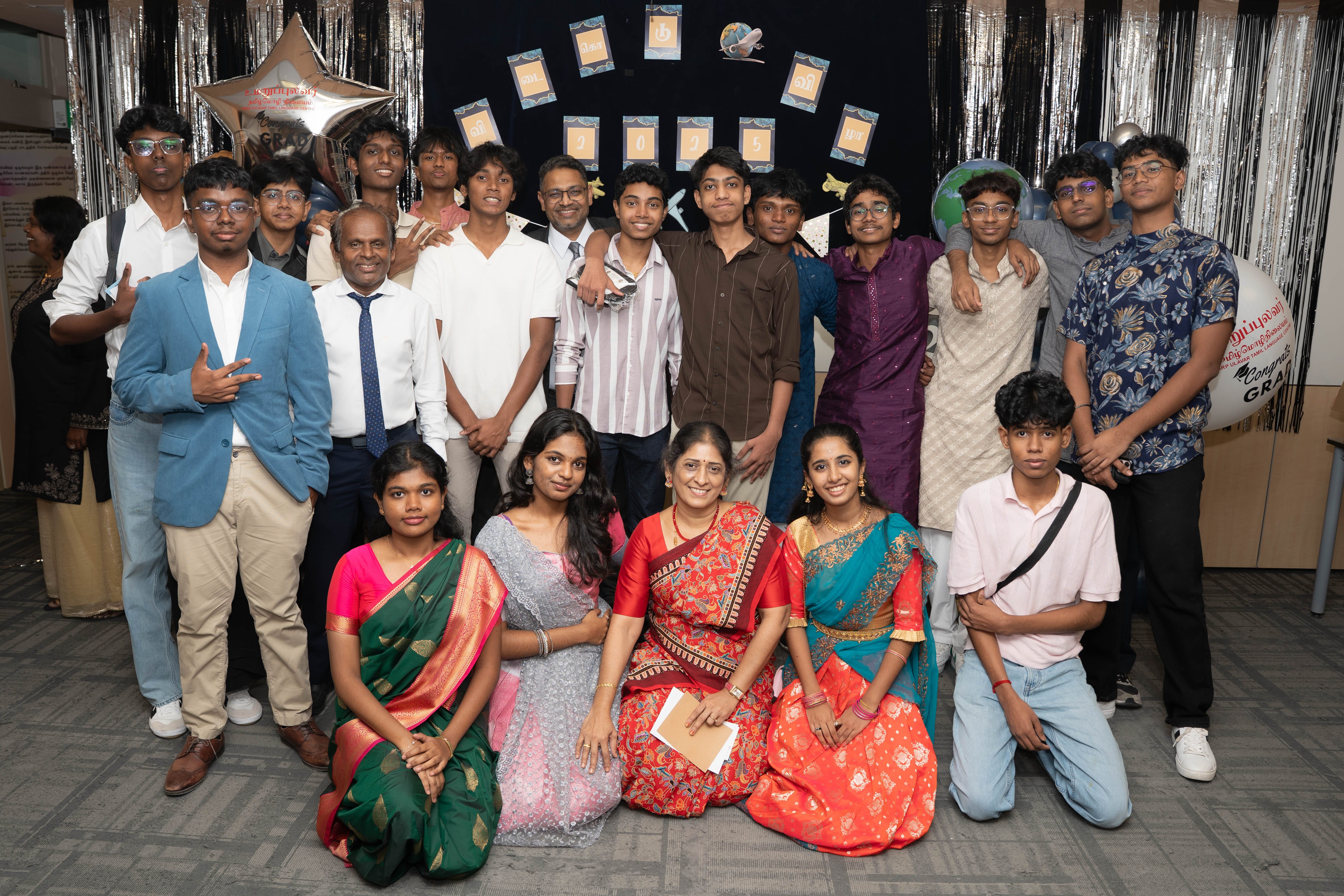 Group photo of students and adults at a decorated event backdrop, some in traditional Indian clothing.