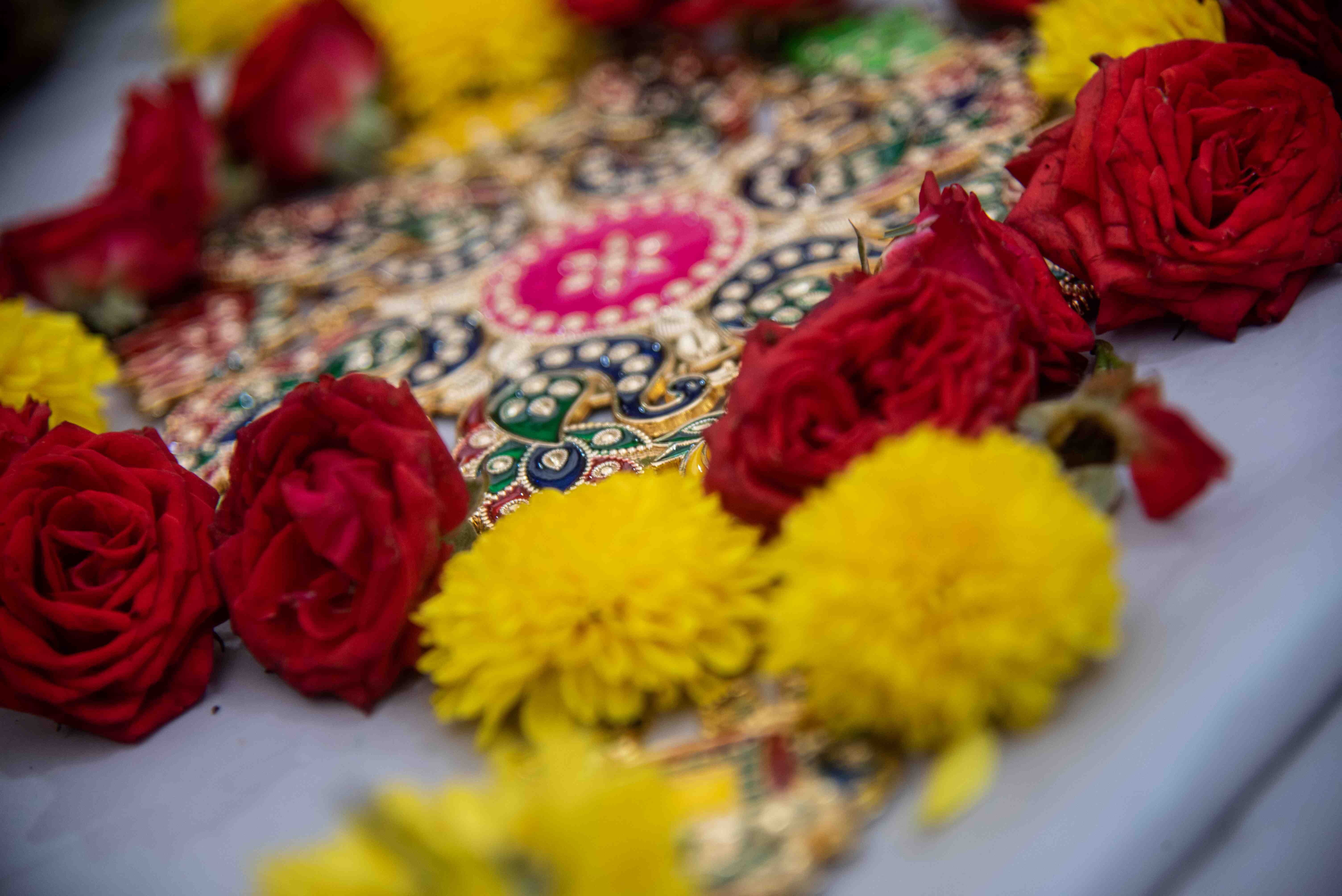 Close-up of red roses and yellow marigolds around a colorful jeweled decorative pattern on gray cloth.