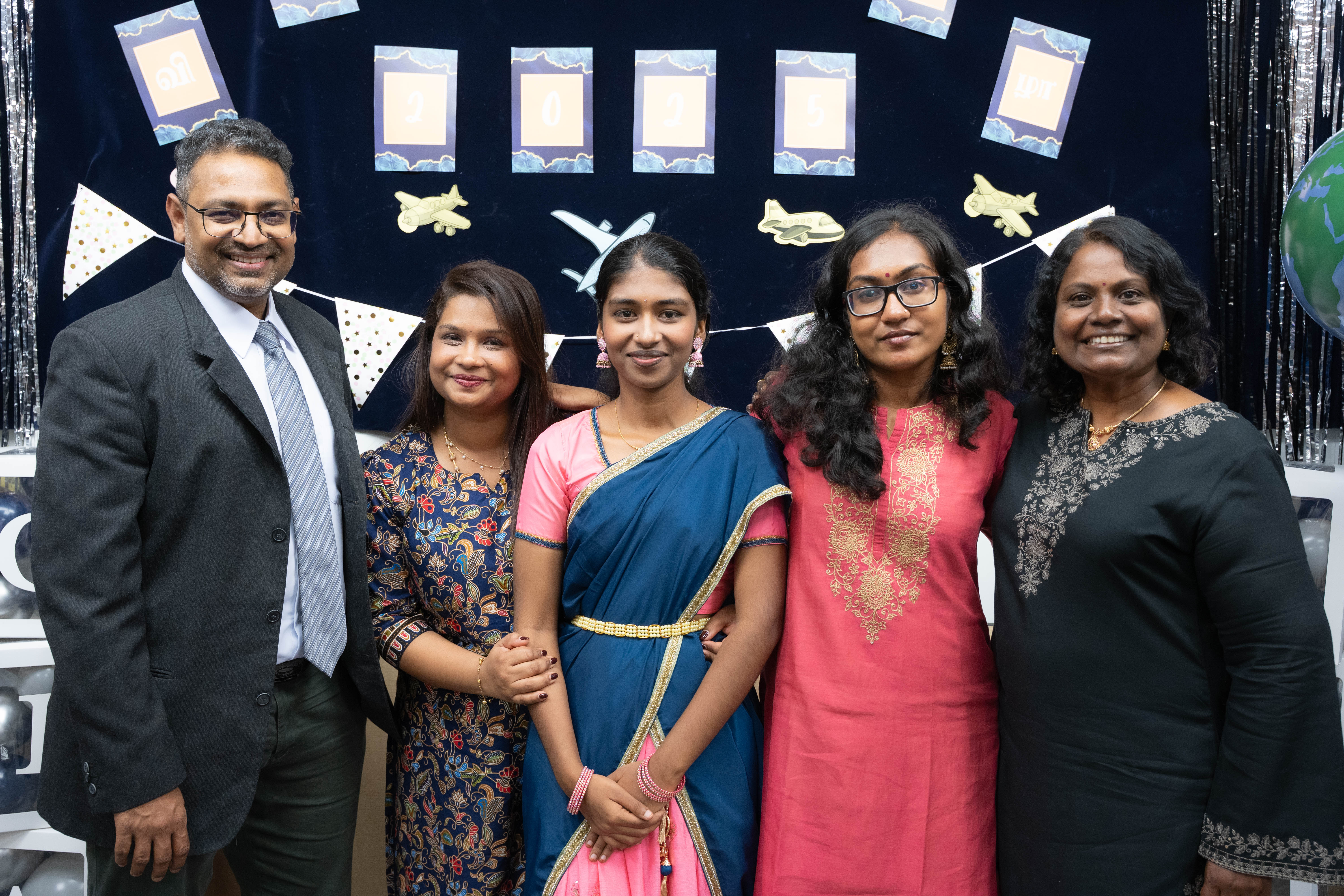 Five adults pose smiling before a decorated 2025 backdrop with airplane cutouts and bunting.