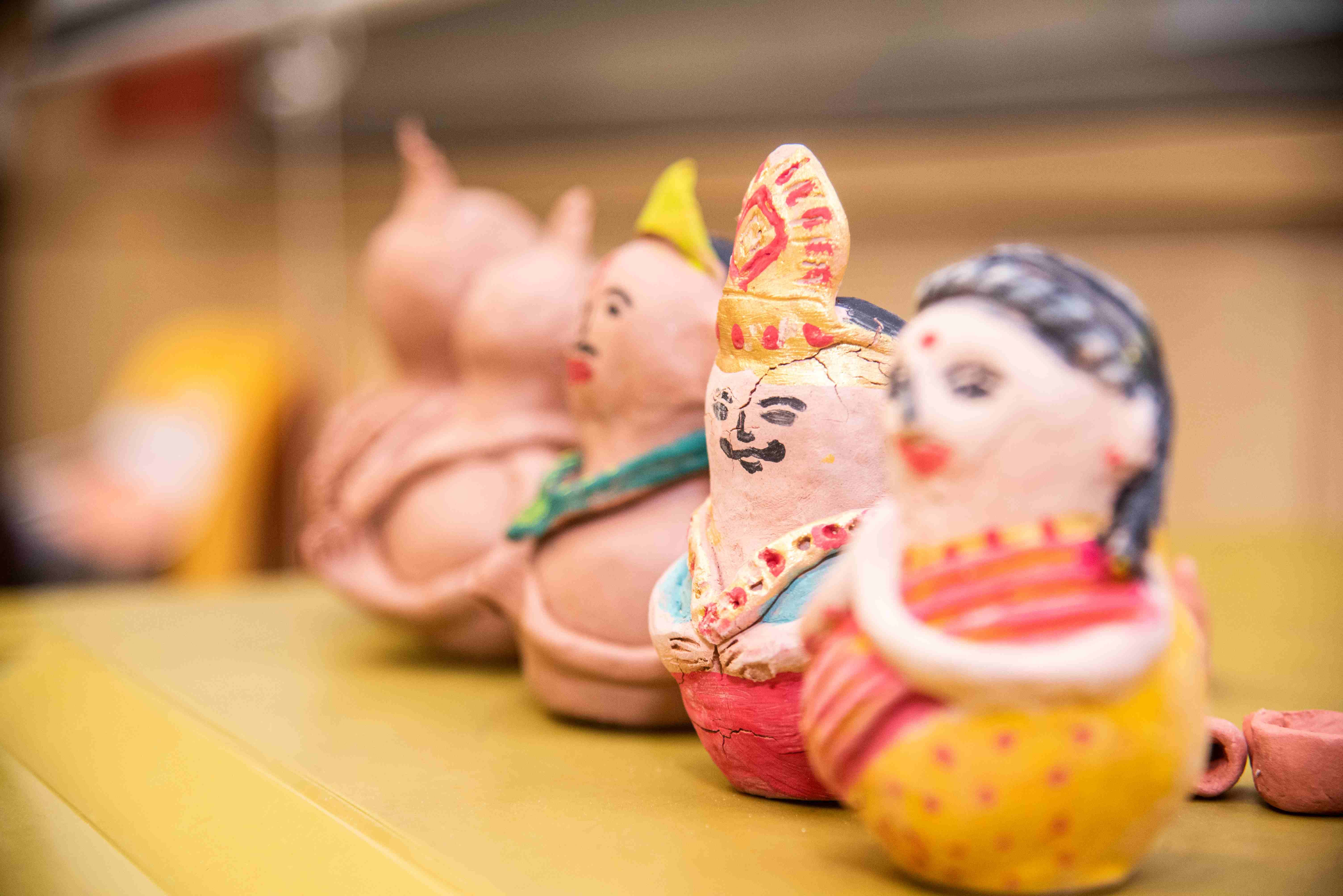 Row of small painted clay figurines on a table, with a woman and a crowned man in front.