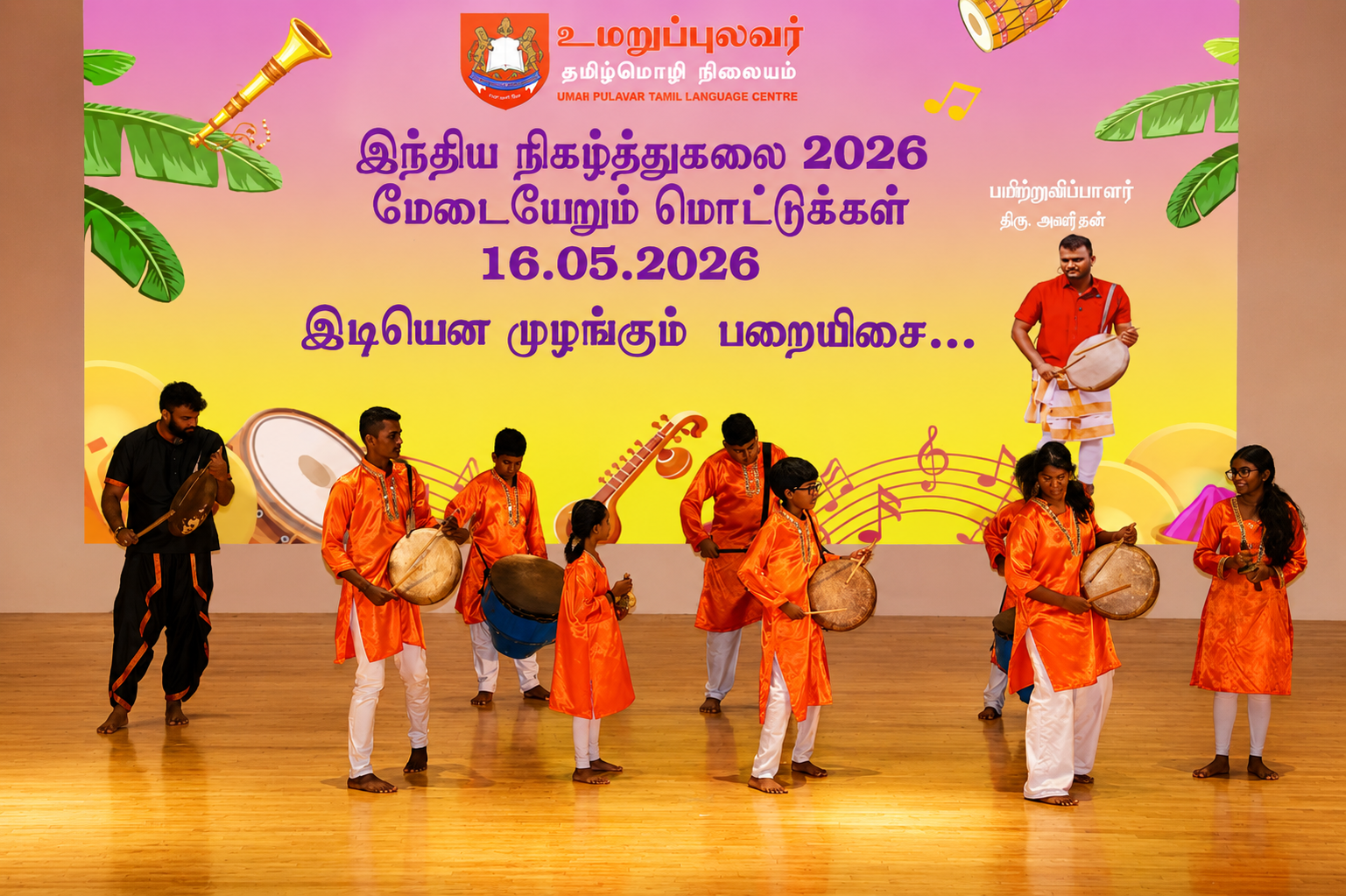 Group in orange costumes performs with drums on stage before Tamil event banner dated 16.05.2026