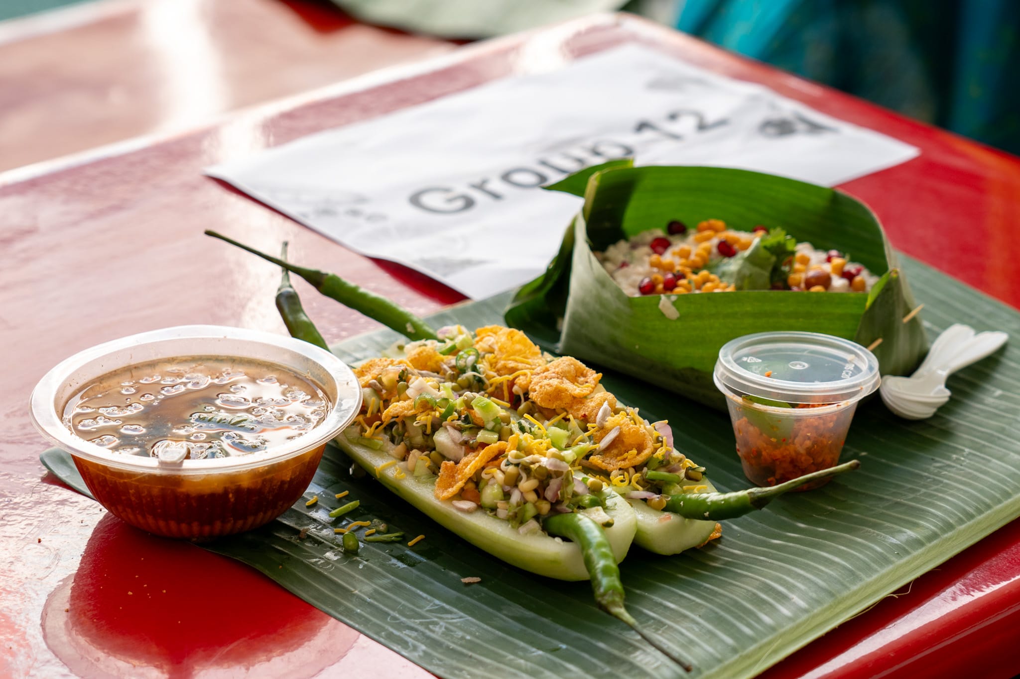 Street food on banana leaf: soup bowl, stuffed cucumber with sprouts, chili cup, and leaf bowl of mixed grains