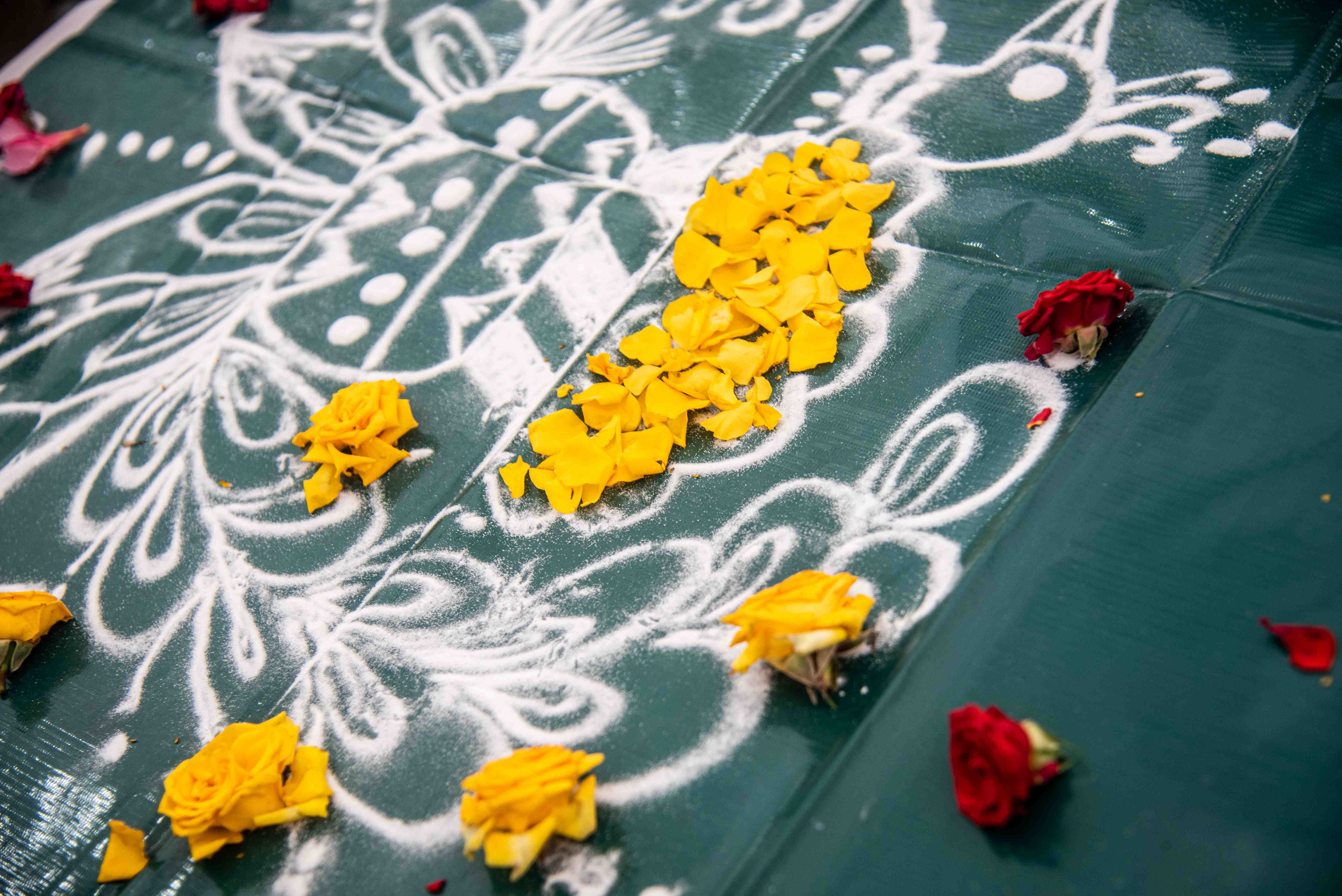 White rangoli-style patterns on green surface, with yellow petals and scattered red and yellow roses.