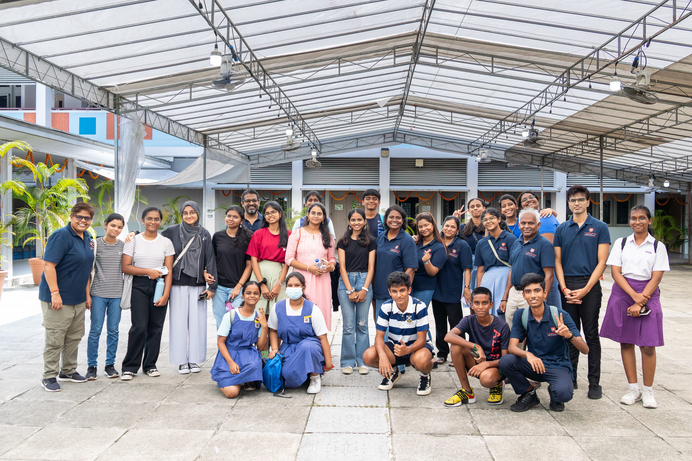 Group of students and adults posing under a covered courtyard, some standing and others kneeling.