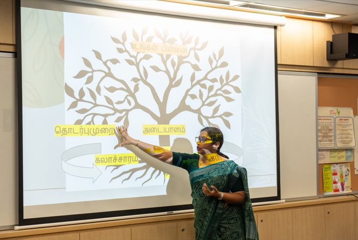 Woman in sari points at projected tree diagram with Tamil labels in a classroom.