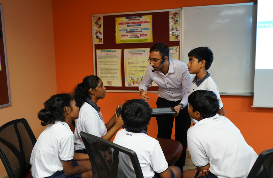 Teacher with headset shows a tablet to five students in white uniforms in a classroom.