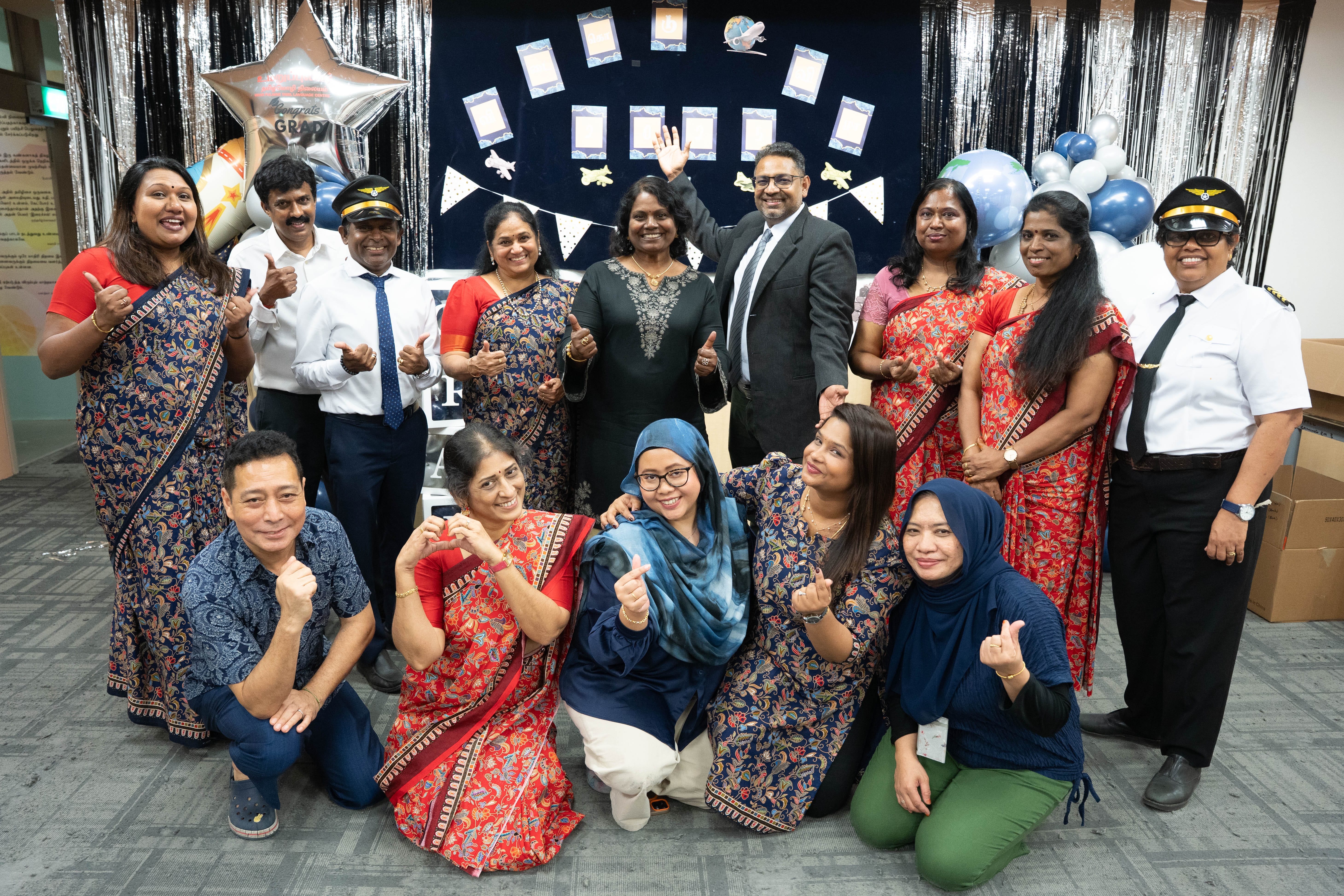 Group of people posing cheerfully at a graduation celebration with balloons, streamers, and a decorative backdrop.