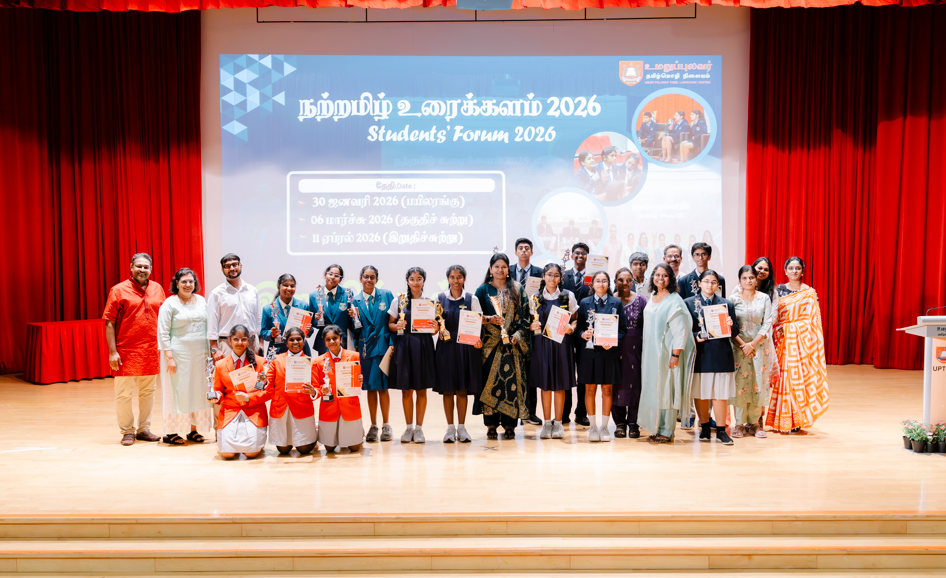 Group of students and adults posing on stage at Students' Forum 2026 event, holding certificates and trophies.