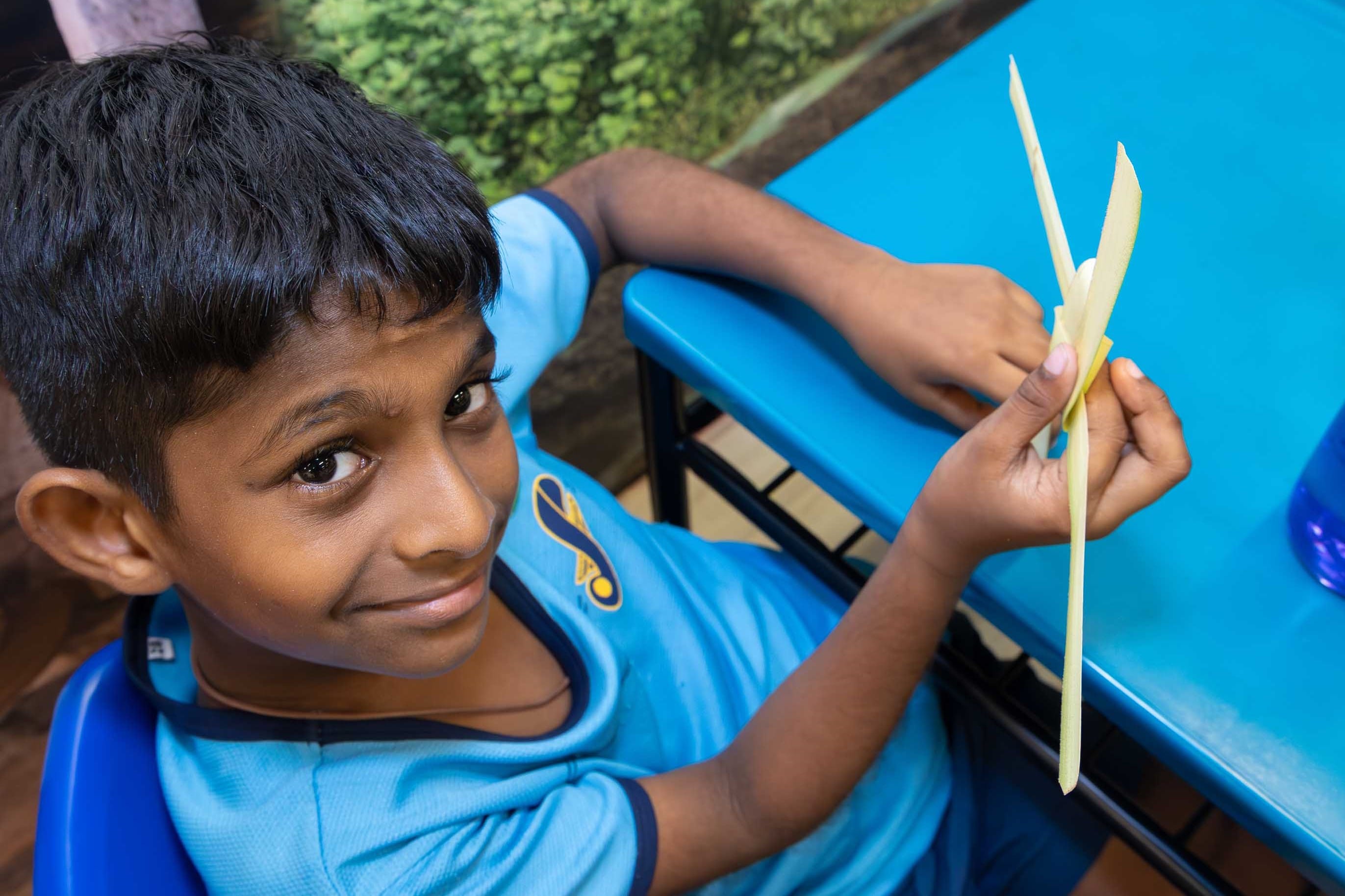 Boy in blue shirt smiles at camera while holding long pale strips at a blue table.