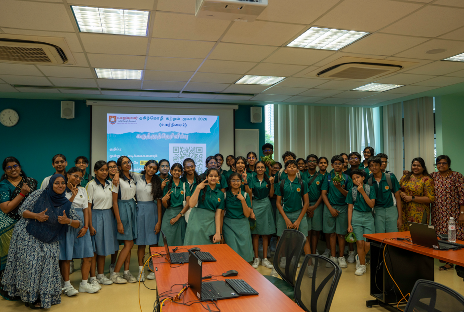 Group of students in green and white uniforms pose in a classroom with a projector screen behind them.