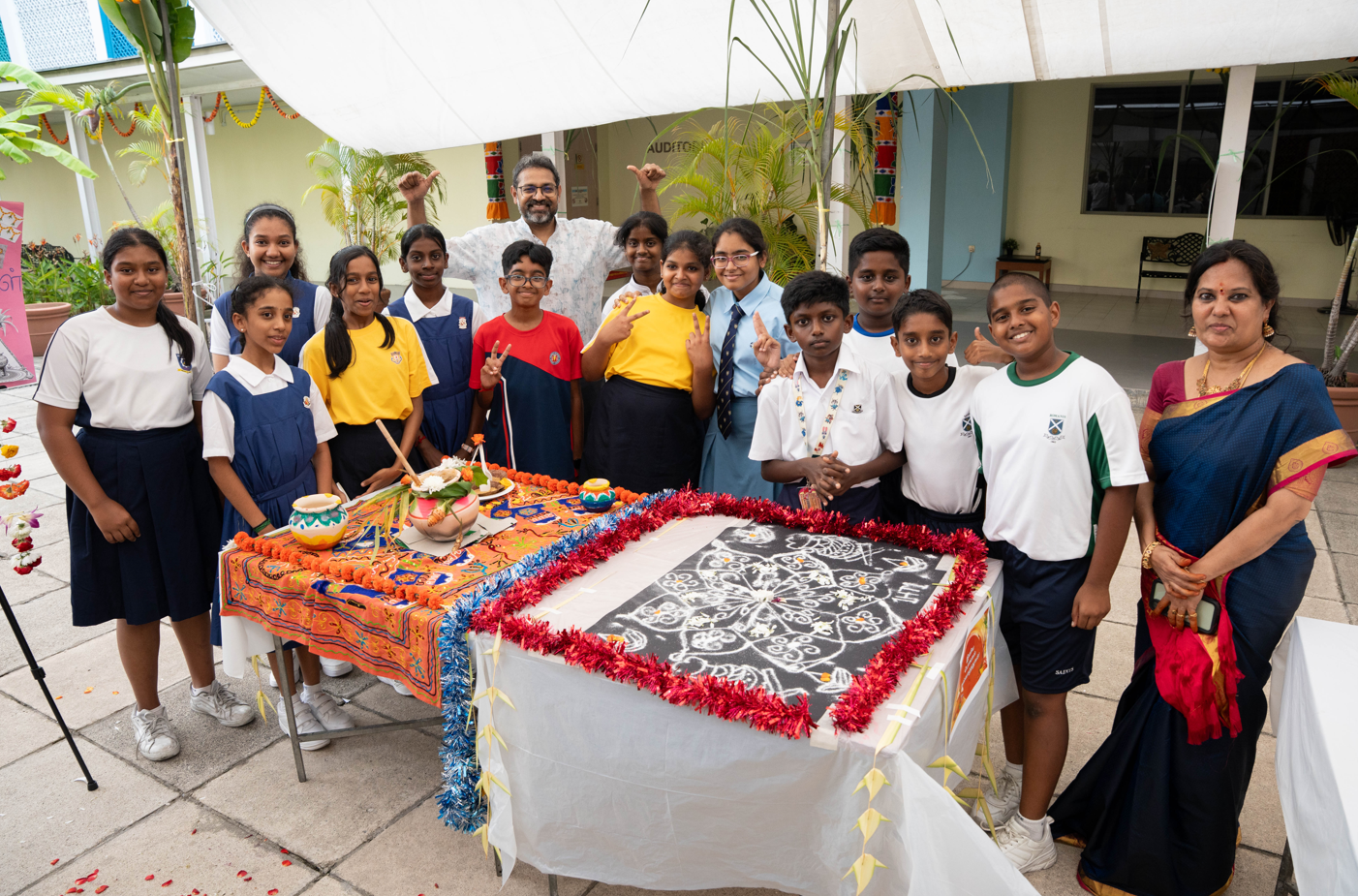 Group of schoolchildren and two adults posing around festive tables with decorated pots and chalk art.