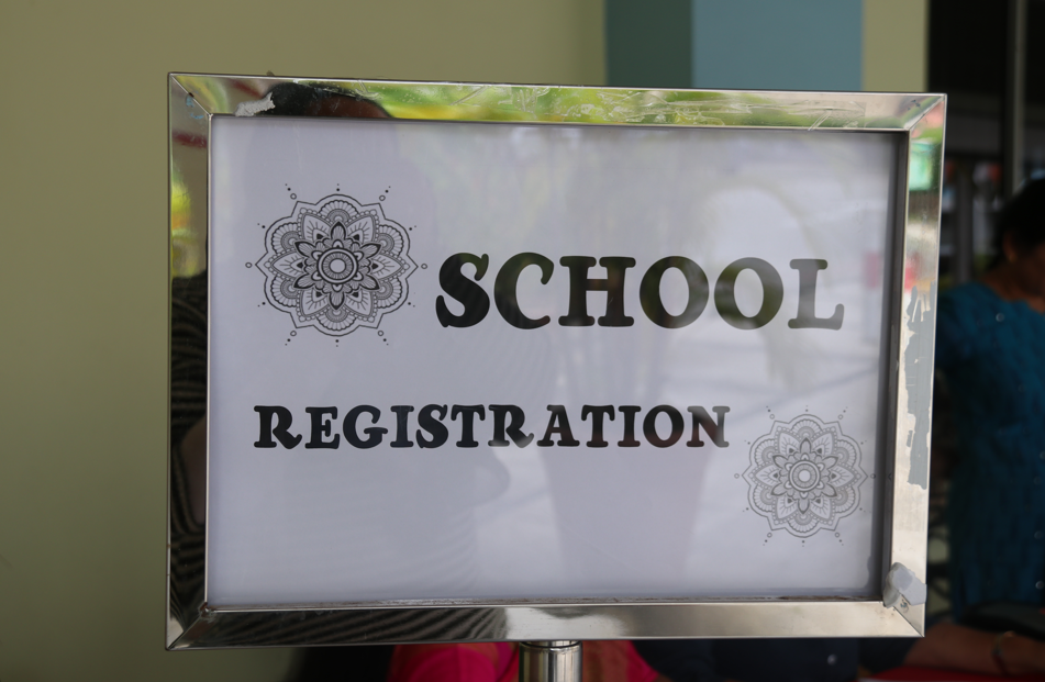 Framed sign on a stand reading SCHOOL REGISTRATION with decorative floral patterns in two corners.