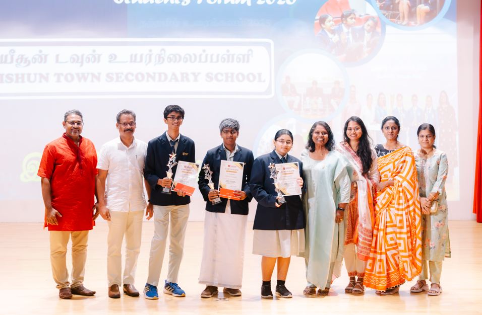 Group on stage with three students holding trophies and certificates, others posing in formal attire.