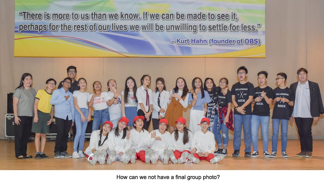 A large group of students and teachers pose on a stage in front of a Kurt Hahn inspirational quote banner.