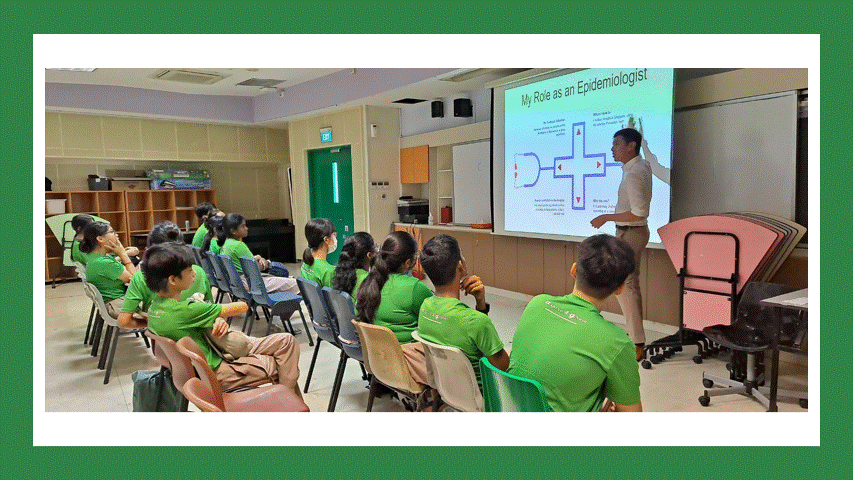 A man presents a slide titled "My Role as an Epidemiologist" to students in green shirts seated in a classroom.