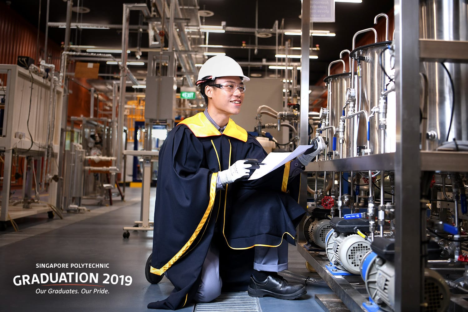 A young man in a graduation gown and hard hat inspects industrial equipment in a factory for Singapore Polytechnic Graduation 2019.