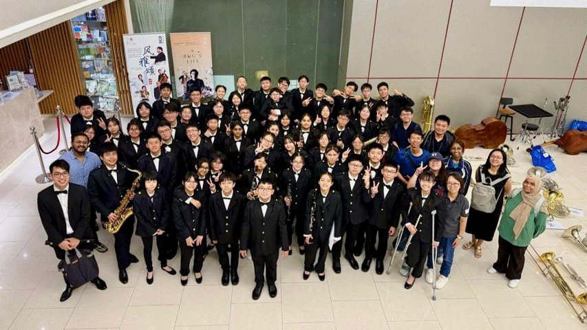 Large group of youth in black formal uniforms posing together indoors, some holding brass and woodwind instruments.