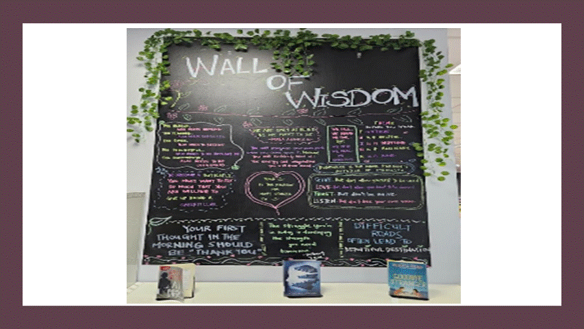 Black chalkboard titled Wall of Wisdom with colorful inspirational quotes, decorated with green vines and three books below.