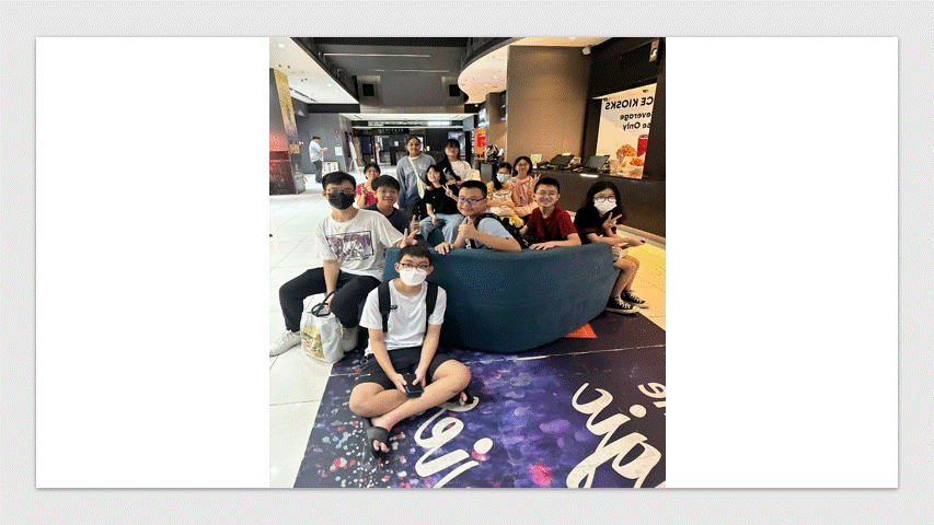 A group of about ten young people wearing face masks pose together inside a mall near a curved sofa.