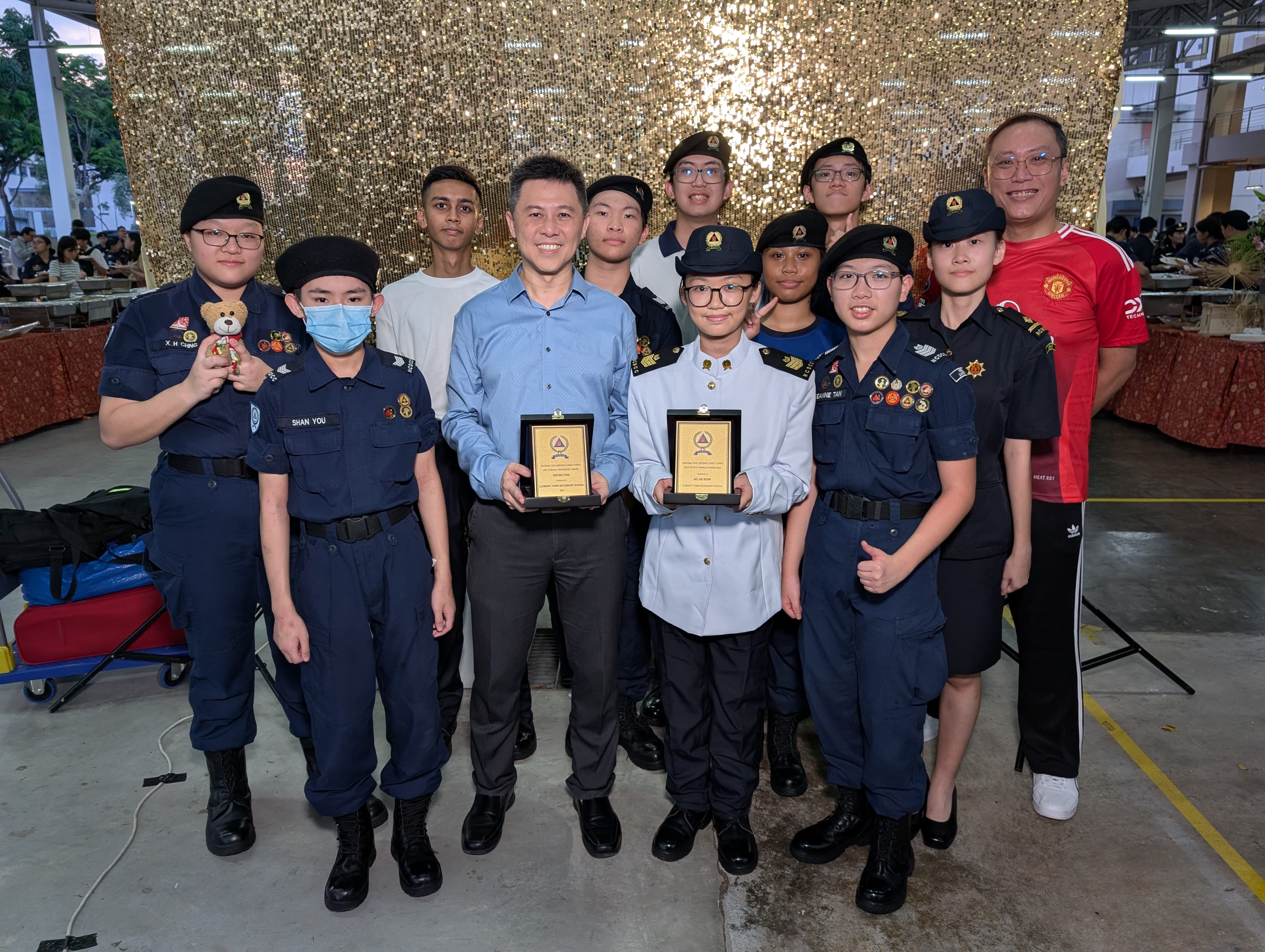 Group of youth in dark uniforms and two adults posing, with two people holding award plaques indoors.