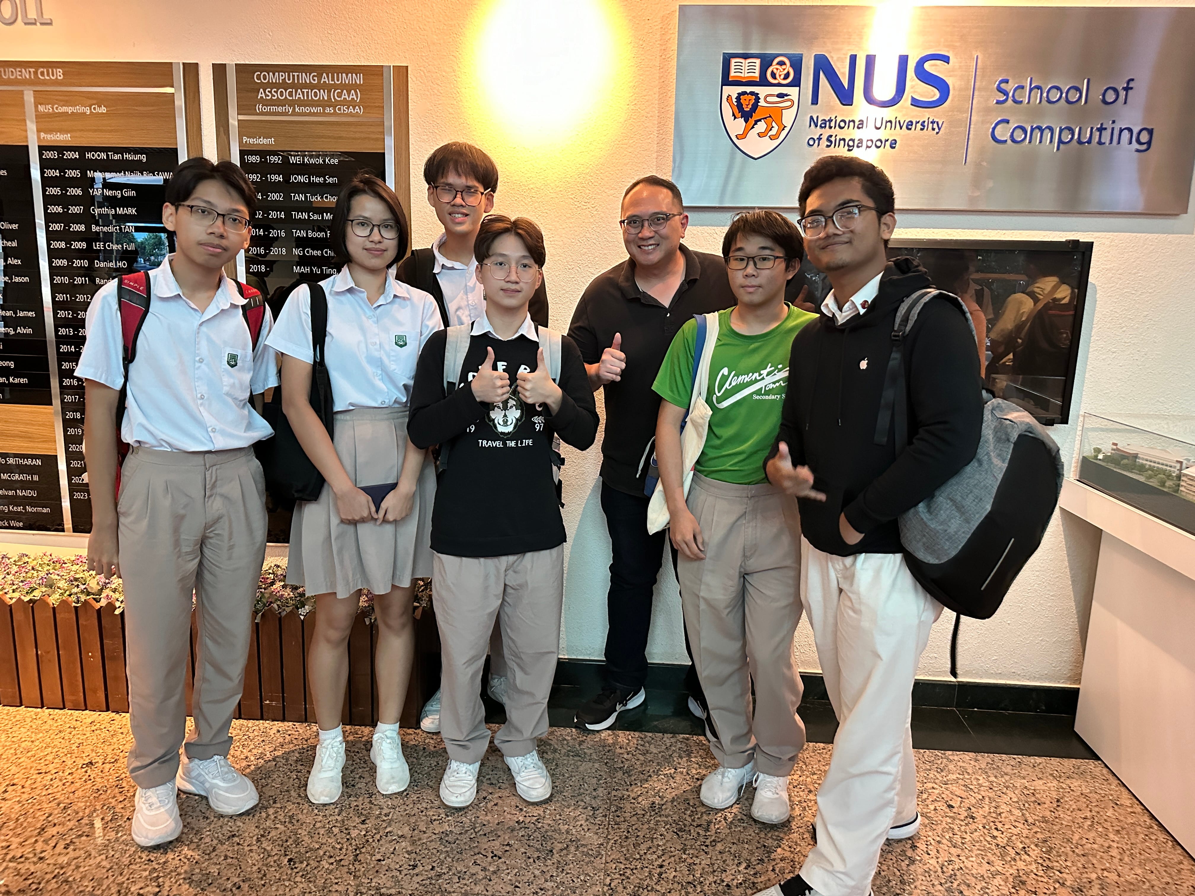 Seven people pose together in front of the NUS School of Computing sign at the National University of Singapore.