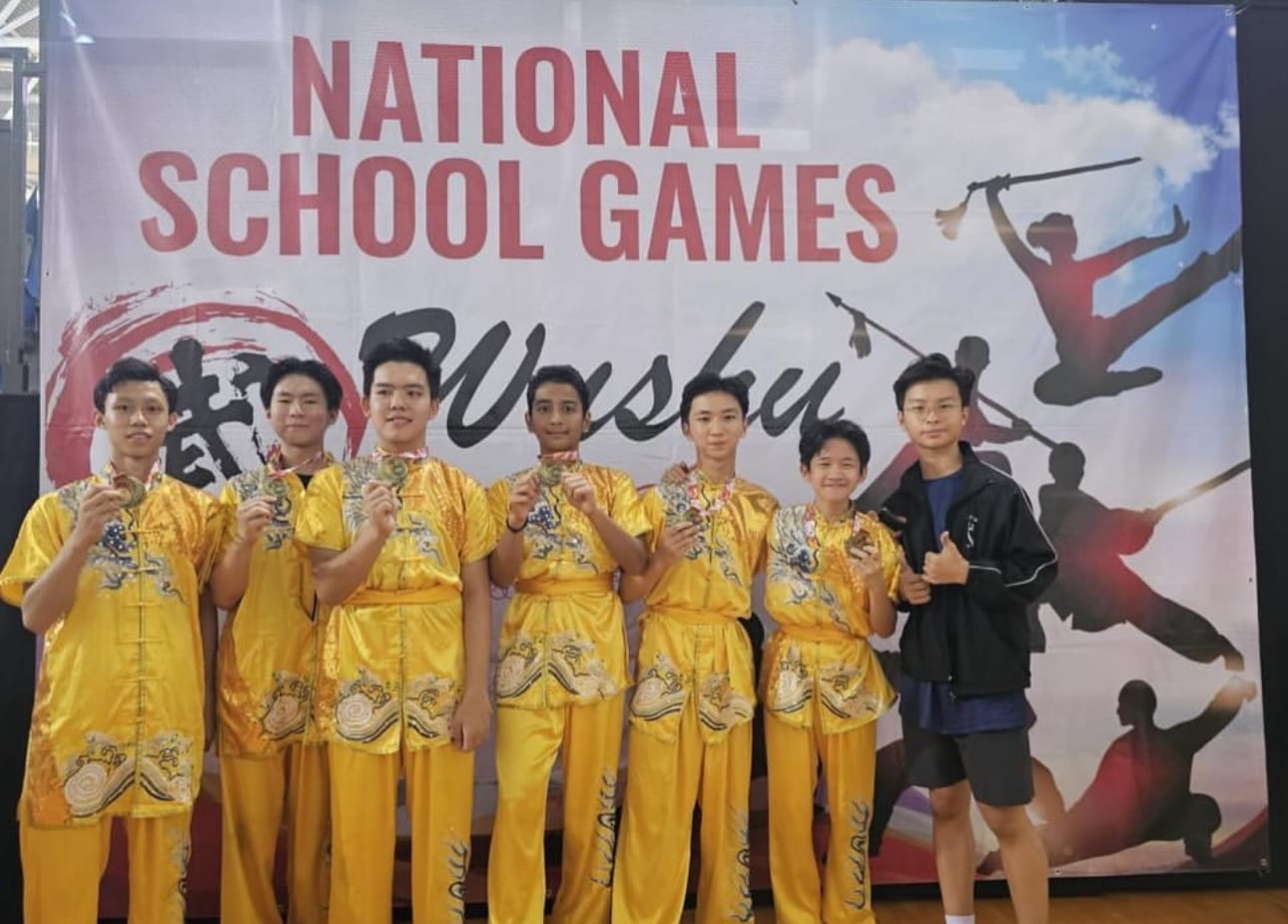 Seven young athletes in gold wushu uniforms display medals in front of a National School Games Wushu banner.