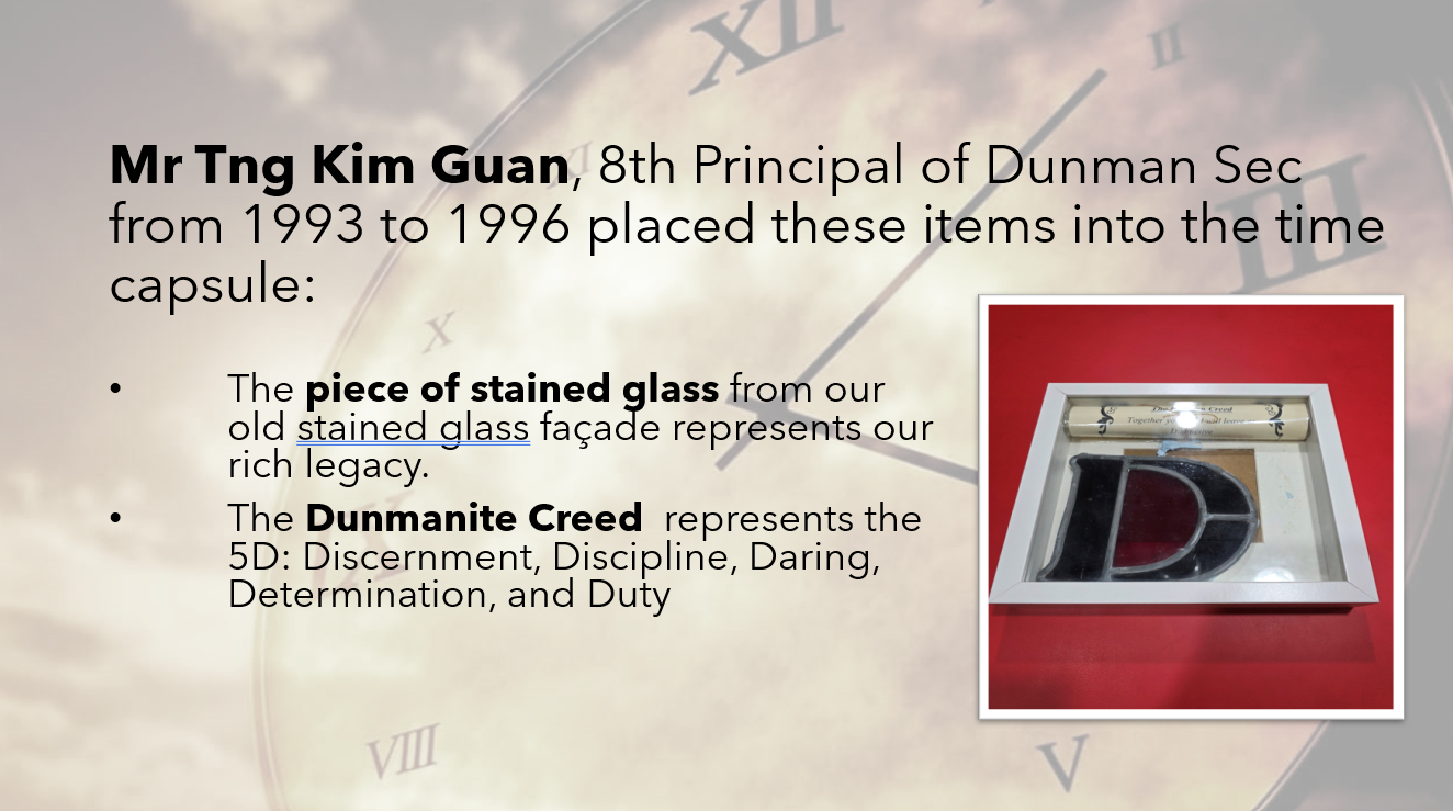 Slide about Dunman Sec time capsule items: a stained glass piece and a rolled Dunmanite Creed scroll in a white tray.