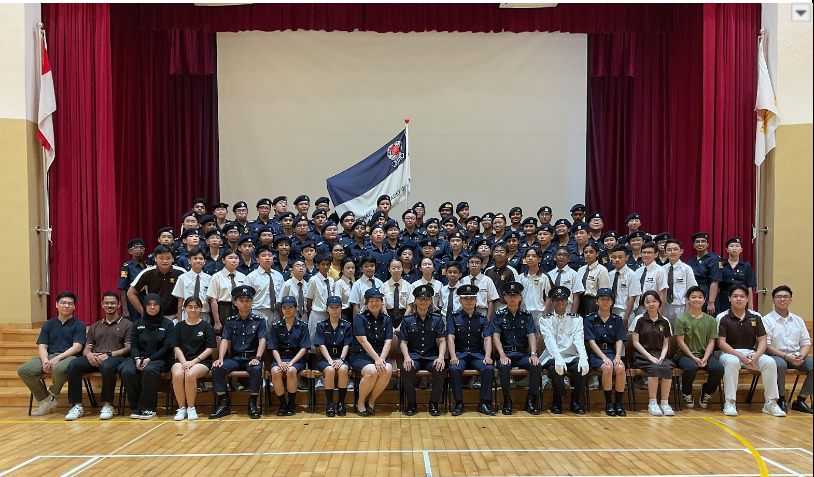 Large group of youth in police cadet uniforms posing for a formal photo in a hall with red curtains.