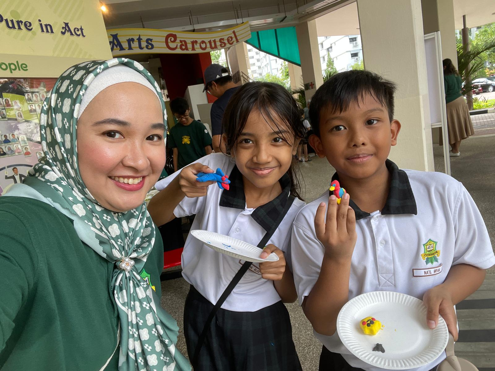 Staff member with two Evergreen Primary School students as they proudly display colourful clay creations made during a hands-on arts activity.