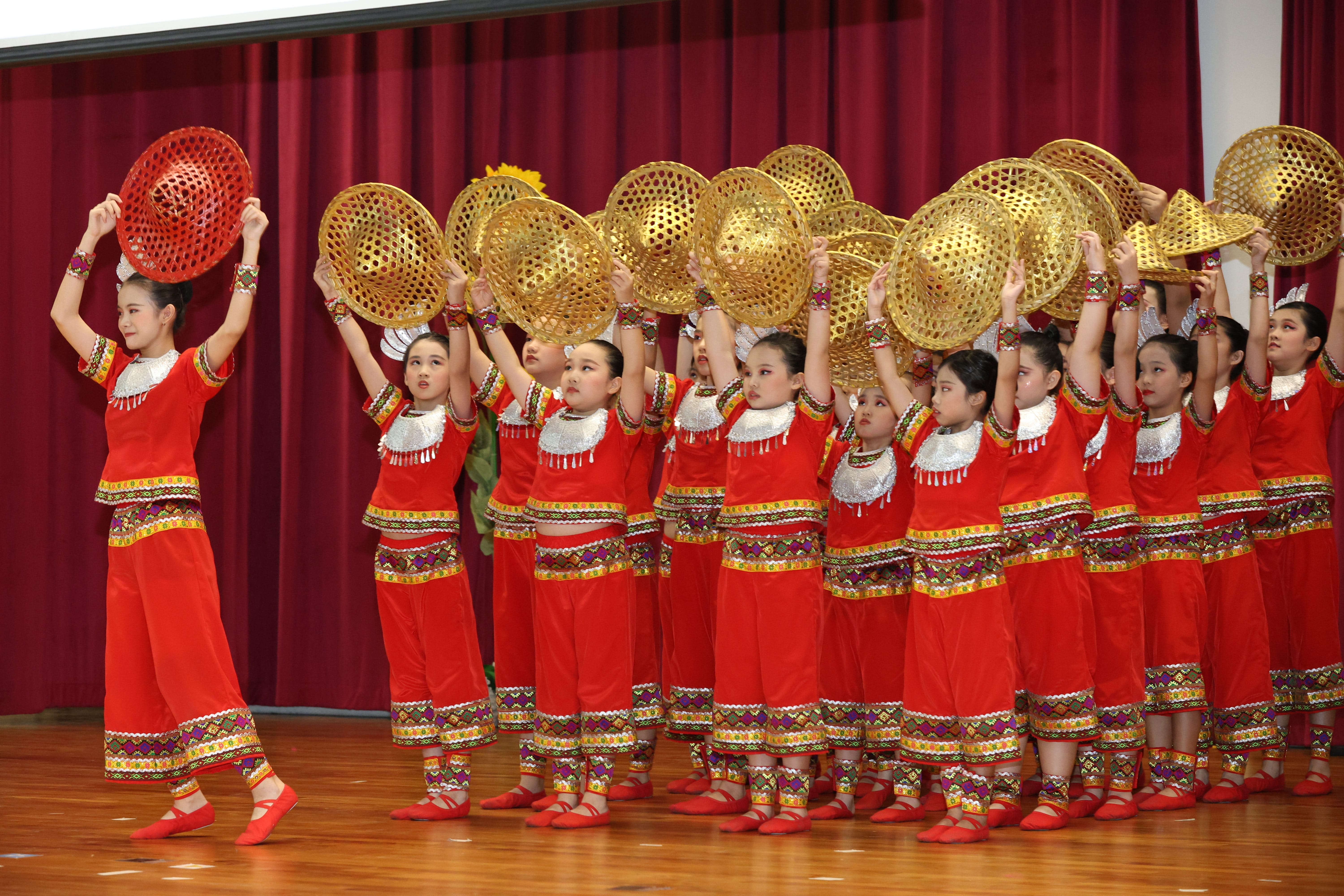 Chinese dance students in red traditional costume performing, holding on to their hats