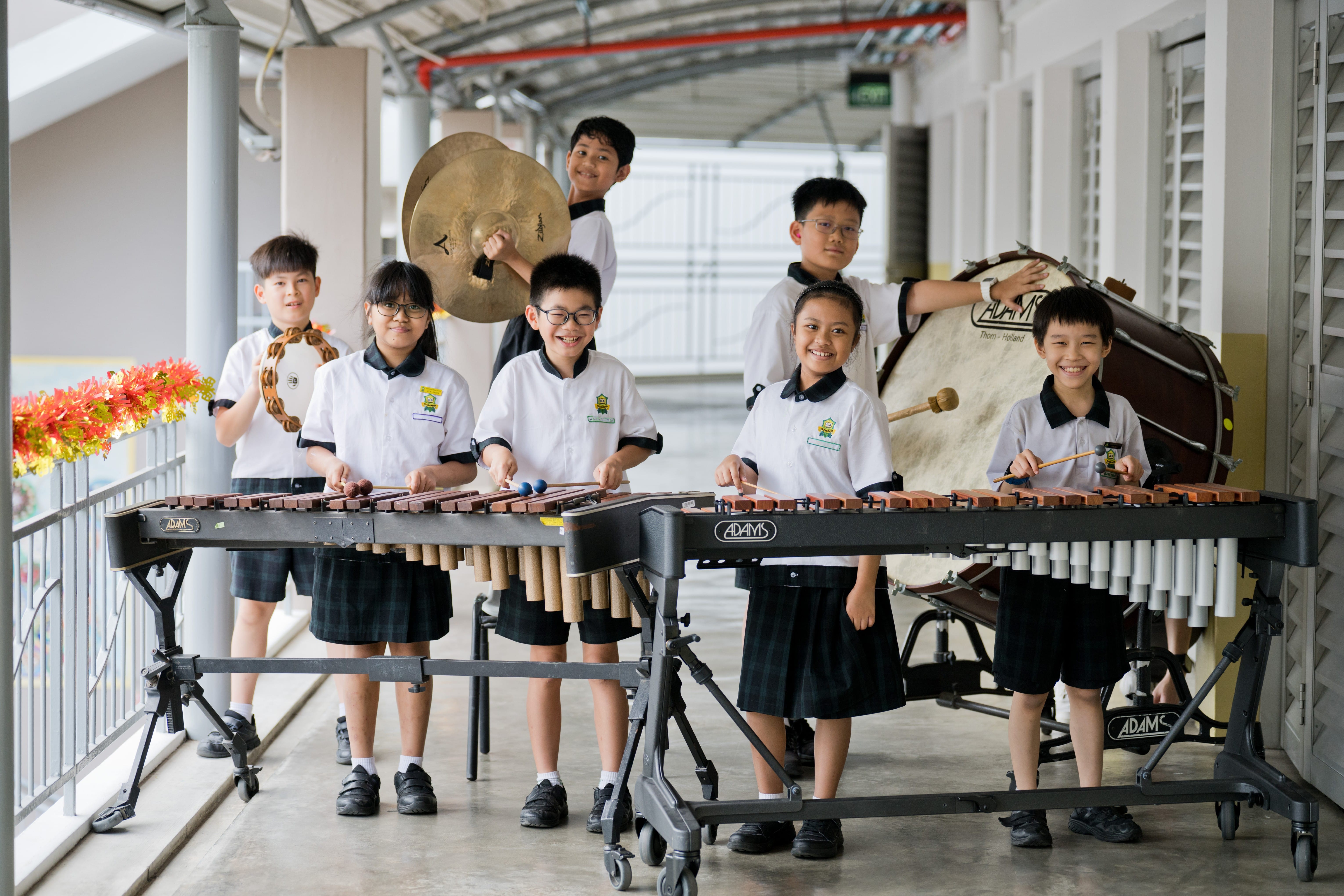 Seven school children in school uniform posing with marimbas, cymbals, and a bass drum