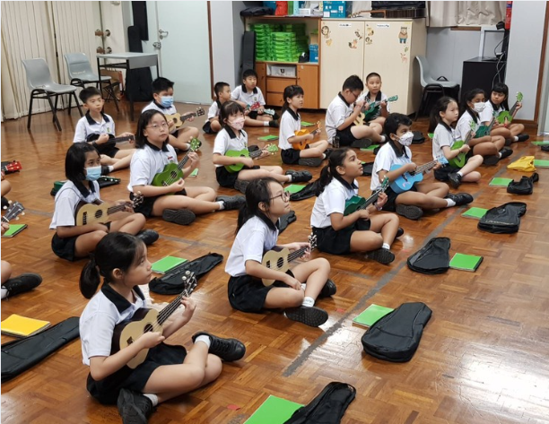 students sit together in a music room, holding colourful ukuleles as they practise playing and learn musical skills together.
