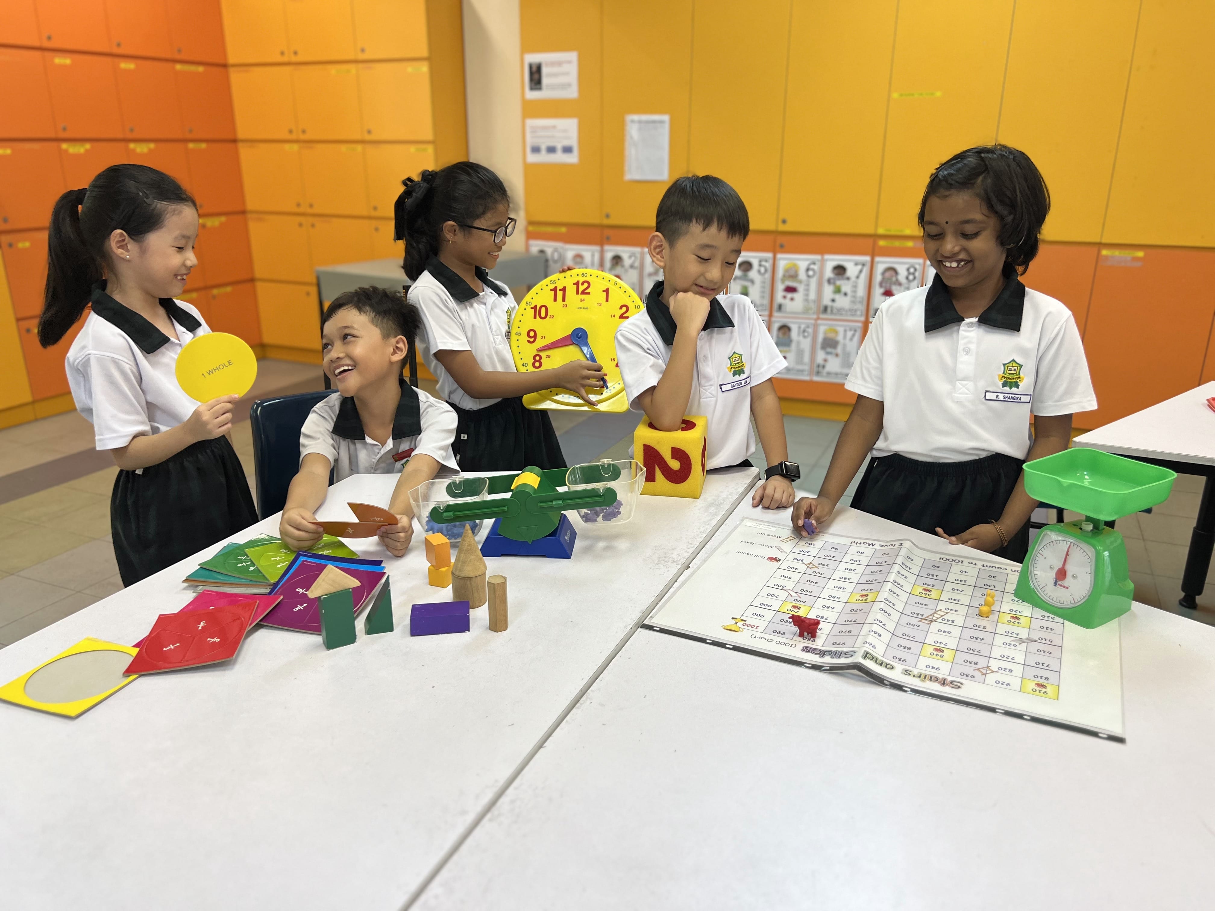 Five young students in school uniforms gather around a table with math learning tools including a clock, scale, and board game.