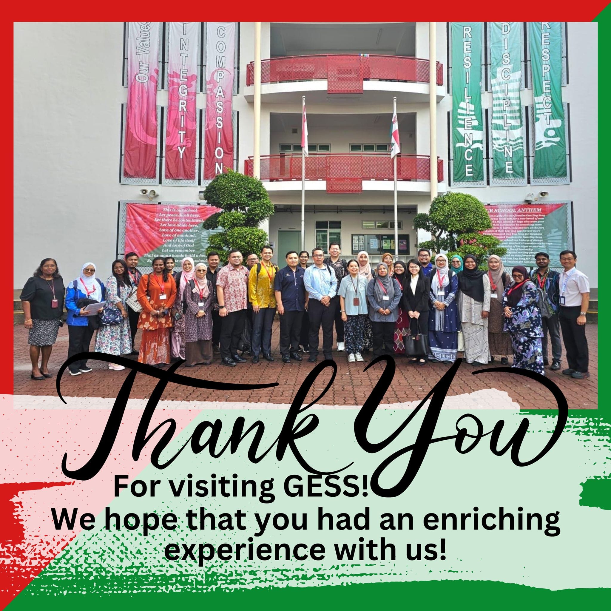 A group of adults posing outside GESS school building with colorful value banners and a Thank You message below.