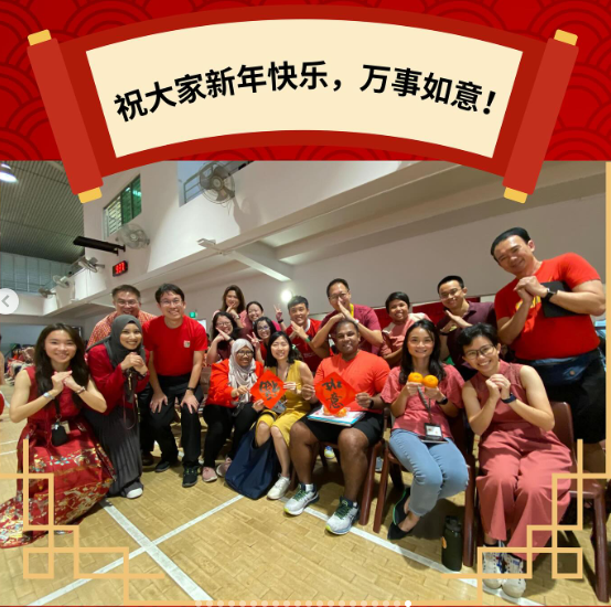 Group of people posing indoors with Chinese New Year decorations and a banner reading happy new year in Chinese.