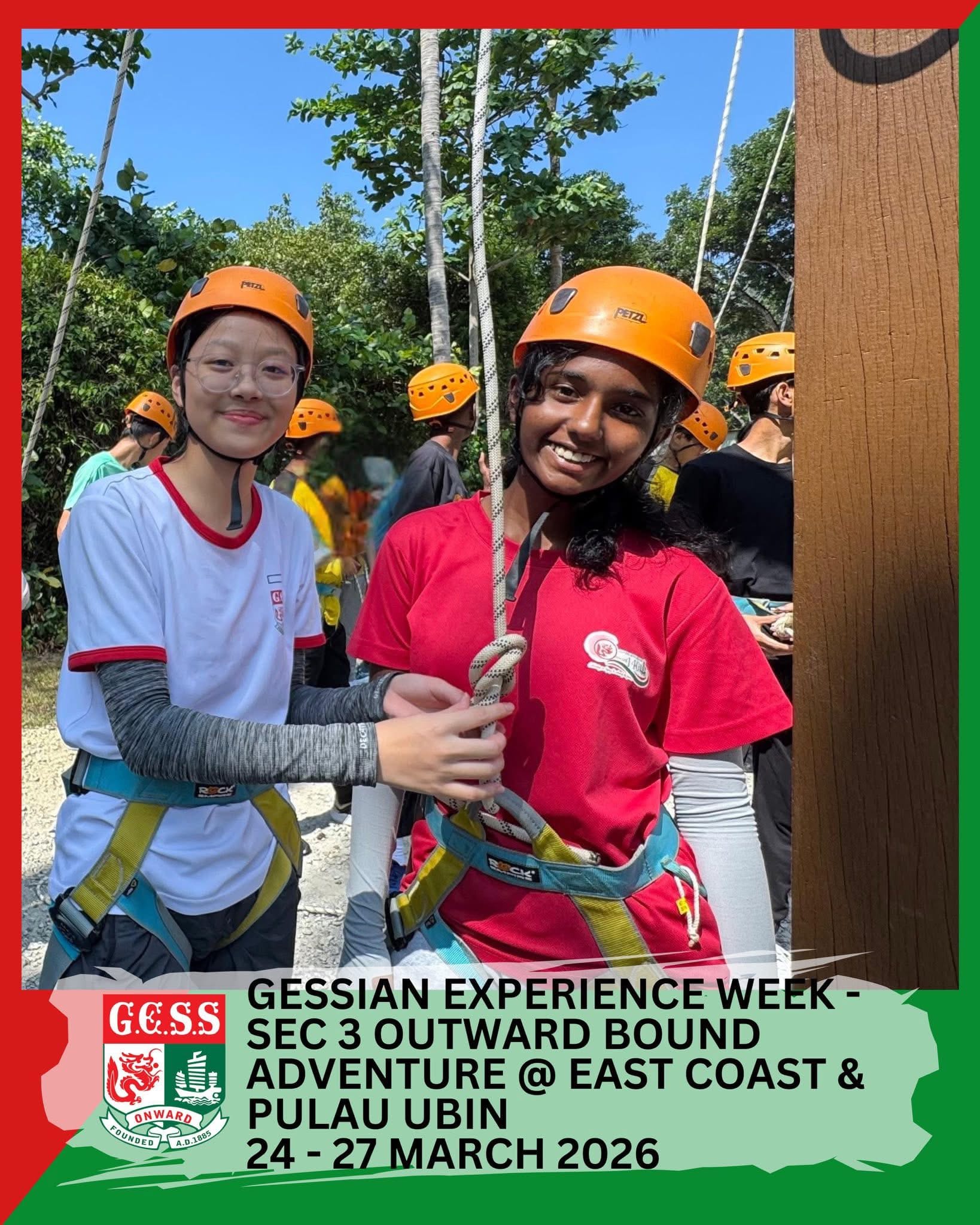 Two smiling students wearing orange helmets and harnesses hold a rope during an outdoor climbing activity.