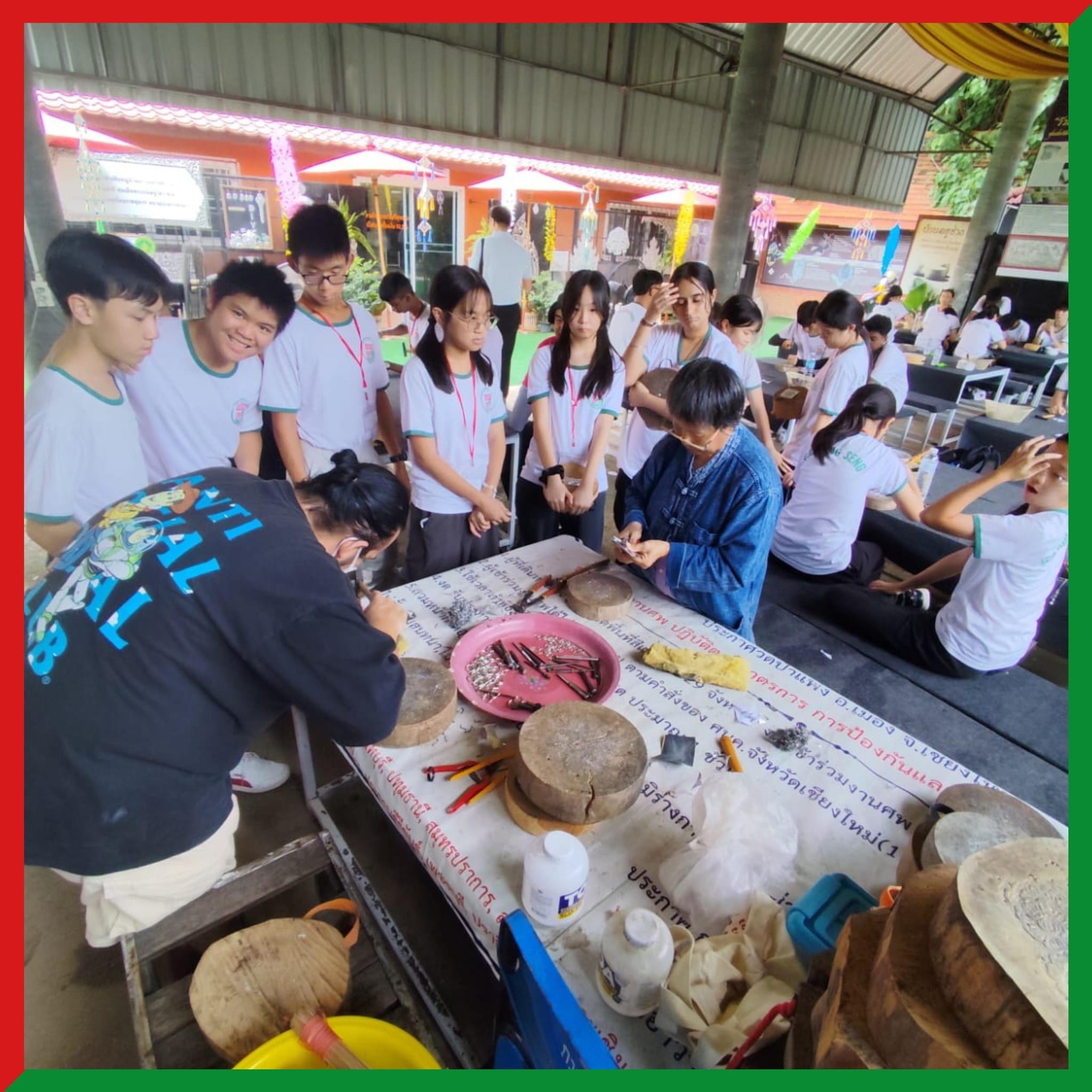 Students in white uniforms gather around a table with tools and bowls during an outdoor craft workshop.