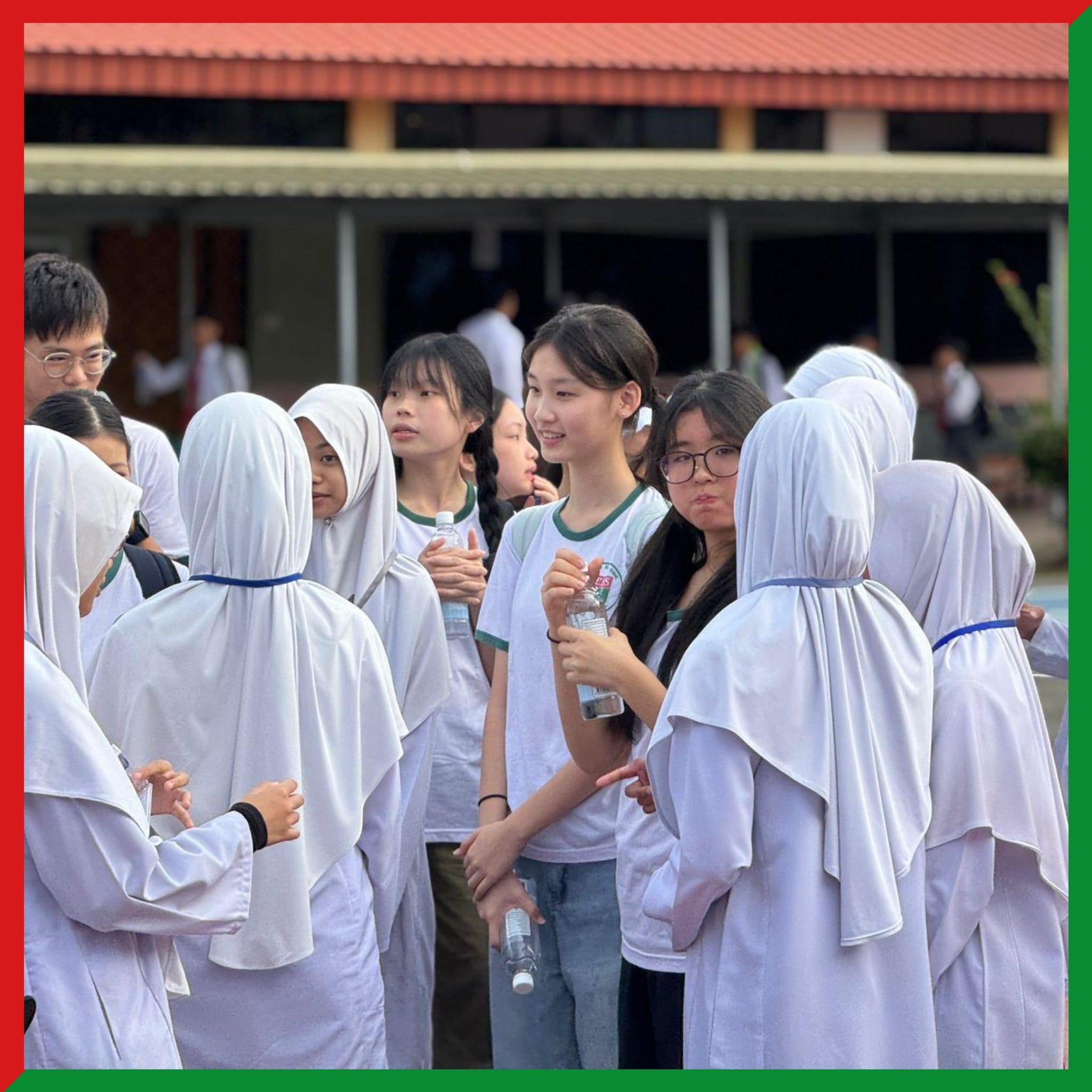 A group of teenage girls, some in white hijabs and some in white t-shirts, gathered outdoors near a school building.