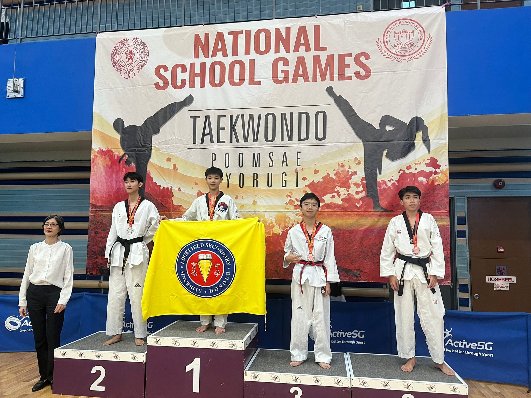 Four taekwondo athletes with medals stand on a podium at the National School Games Taekwondo competition.