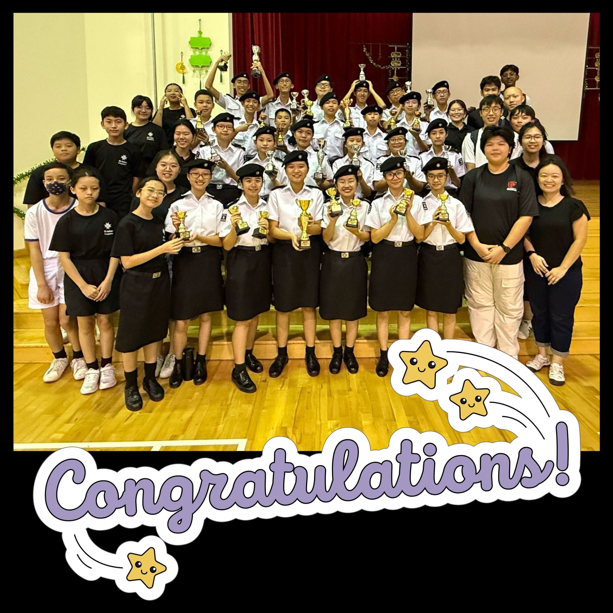 A large group of uniformed students holding trophies pose together indoors with a Congratulations text overlay.