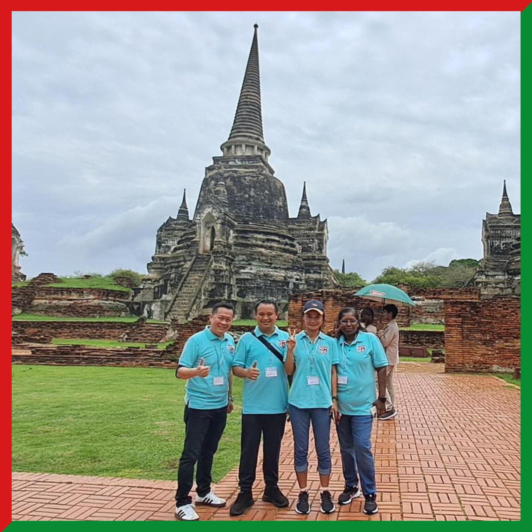 Four people in matching teal polo shirts pose in front of a large ancient Thai temple with tall stone spires.
