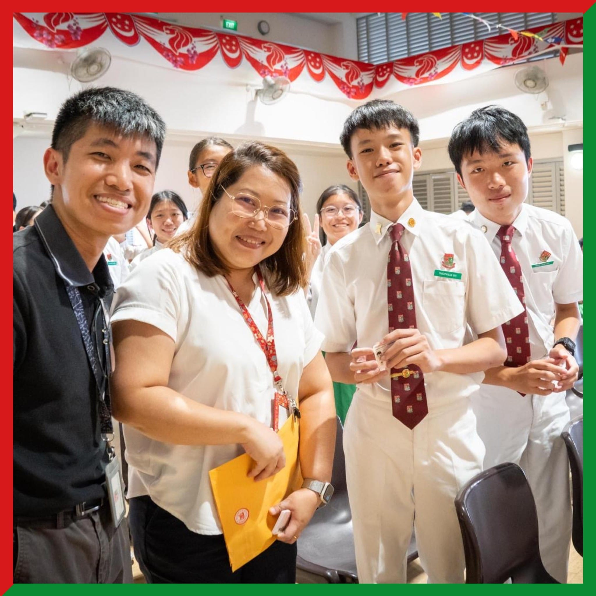 Four smiling people pose together indoors at a school event with red festive decorations overhead.