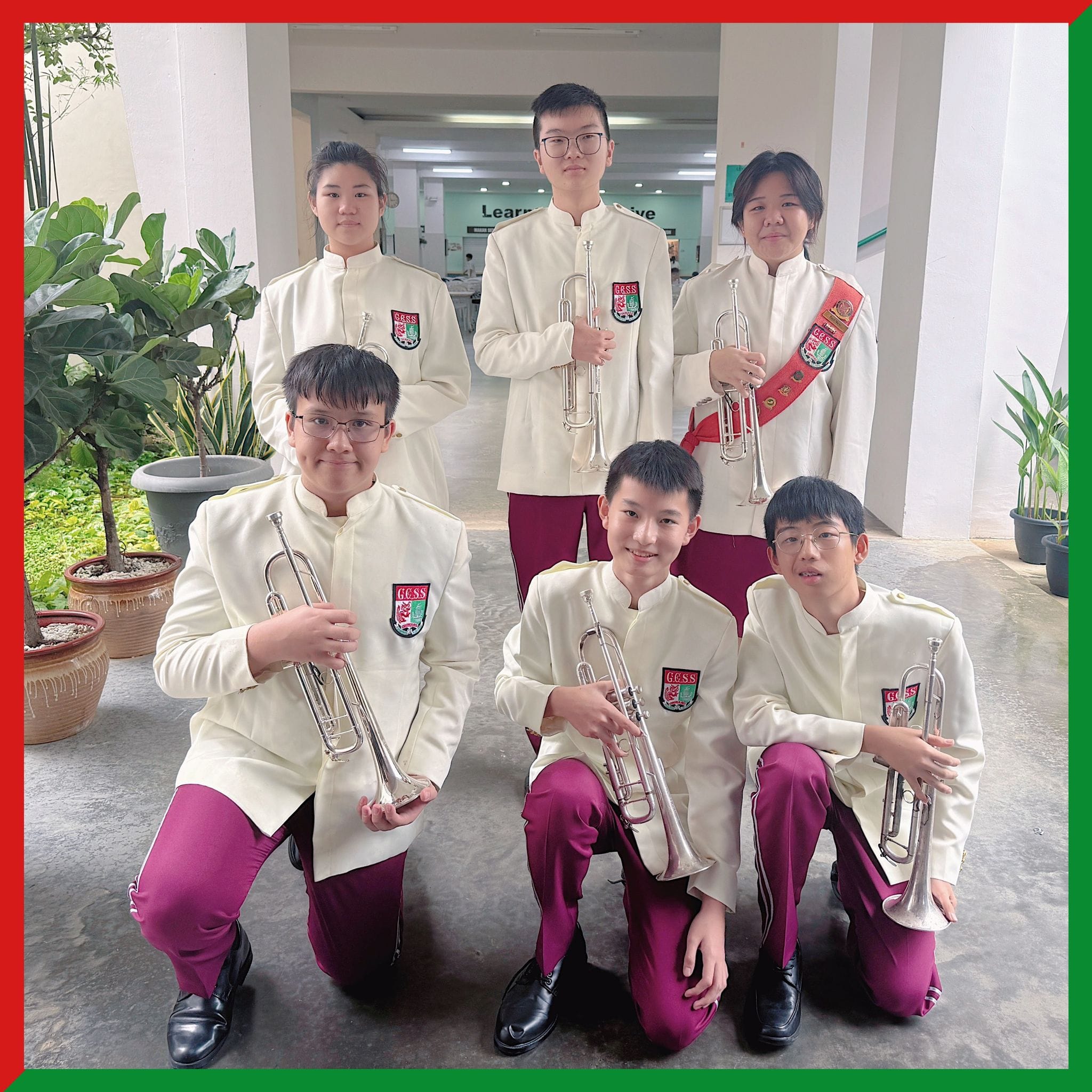Six students in white and maroon school band uniforms holding trumpets, posing in two rows indoors.