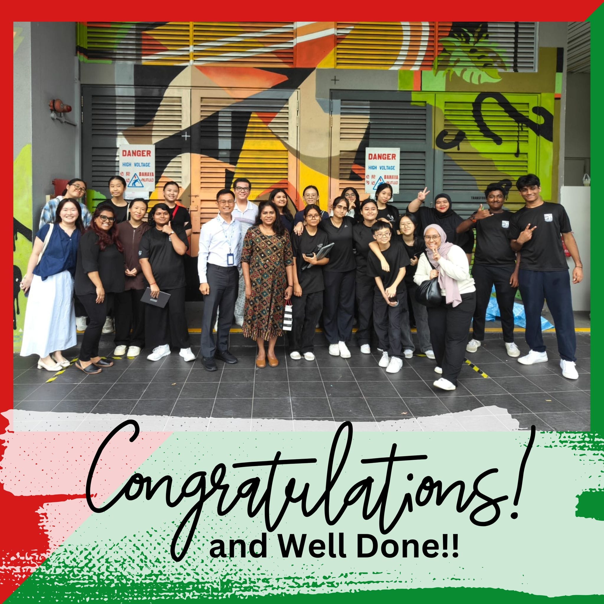Group of about 20 people posing in front of a colorful mural with text reading Congratulations and Well Done.