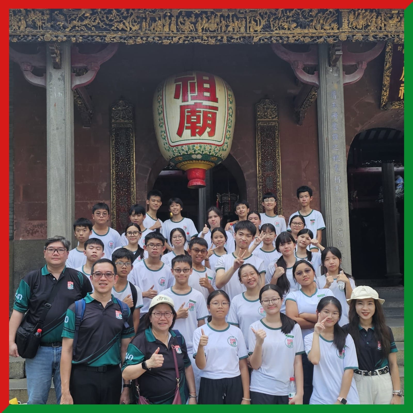 A large group of students in white uniforms poses in front of a traditional Chinese temple with a large lantern.