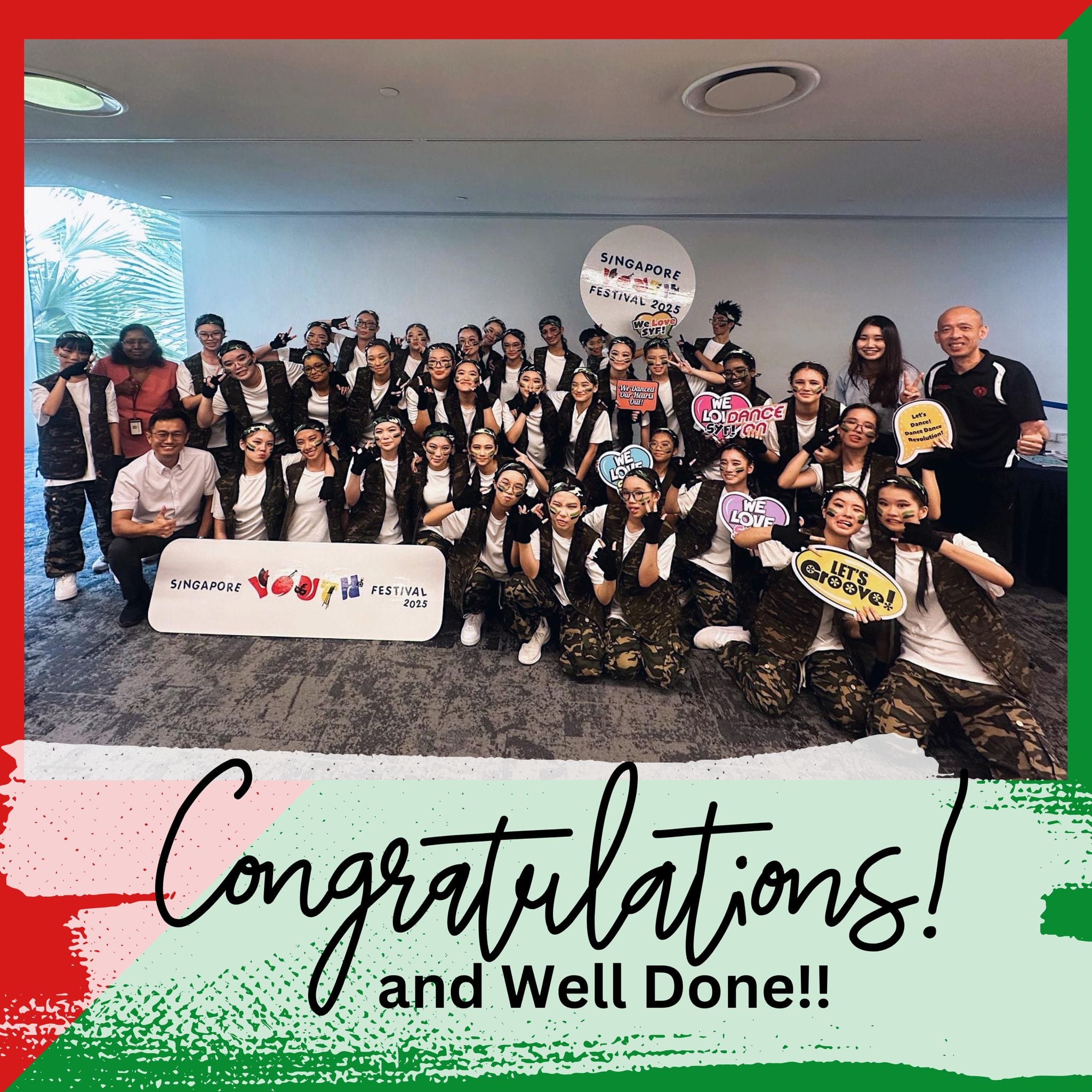 Large group in camouflage vests posing at Singapore Youth Festival 2025 with props and a Congratulations text below.