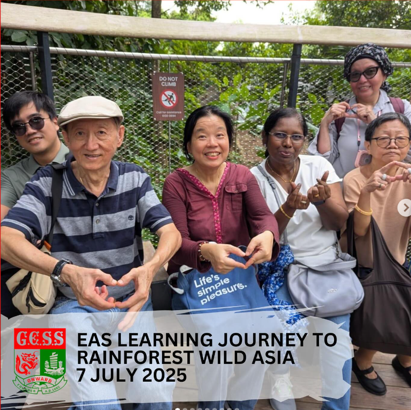 Six people smile and form heart shapes with their hands on a walkway surrounded by greenery.
