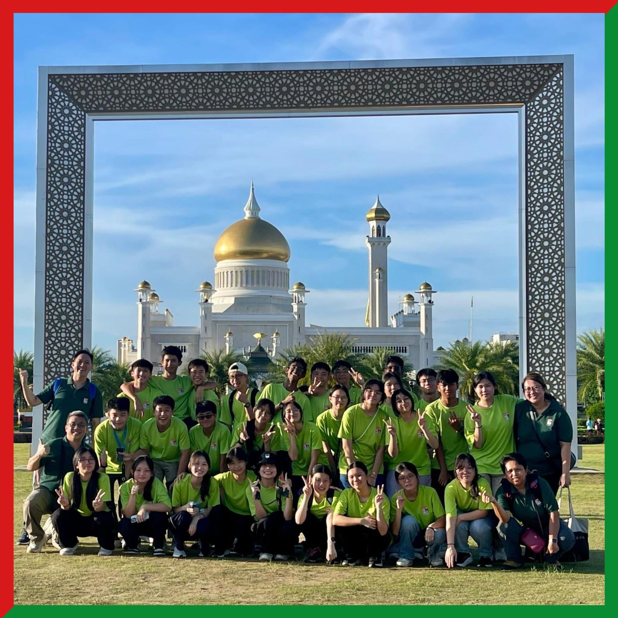A large group in green shirts poses before a white mosque with golden domes, framed by a decorative arch.