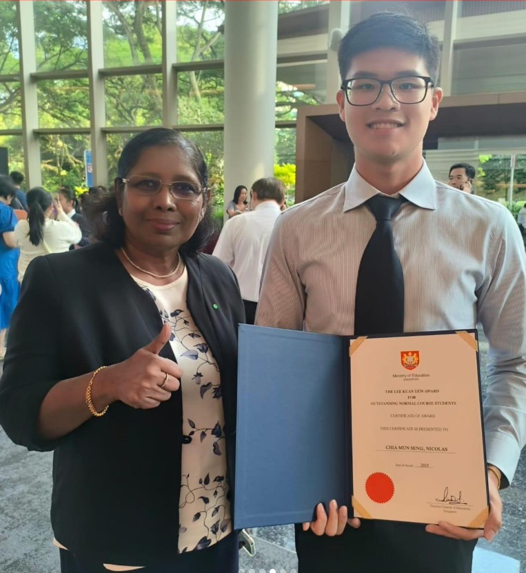 A woman gives a thumbs up beside a young man holding a Lee Kuan Yew Award certificate outdoors.